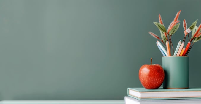 Red Apple and Colorful Pencils on Stacked Books Against a Green Wall photo