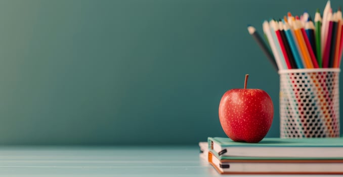 Red Apple on Stack of Notebooks With Colorful Pencils in Container Against a Green Background photo