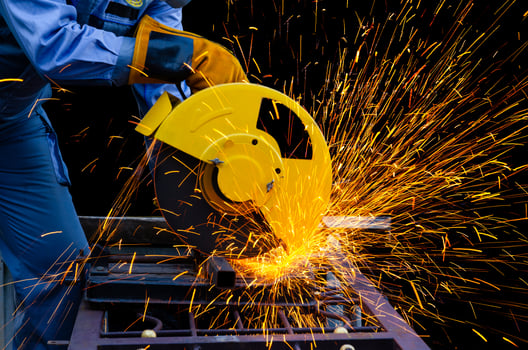 Worker man in blue uniform with yellow leather gloves cutting metal pipe by electric circular abrasive saw with sparks. Metal working with personnel protective equipment. photo