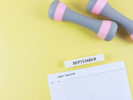 flat lay of habit tracker book, wooden calendar September, gray pink dumbbells, on yellow background with copy space. Self development and active lifestyle concept. photo