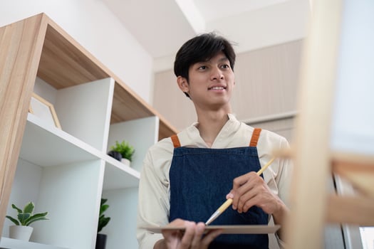 Young Male Artist Painting on Canvas in Modern Studio with Shelves and Plants photo