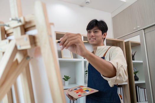 Young Male Artist Painting on Canvas in Modern Studio with Shelves and Plants in Background photo