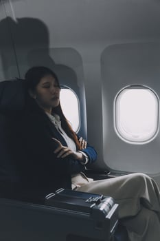 Photo of a frustrated woman sitting on an airplane with her head in her hands. Asian woman sitting in a seat in airplane