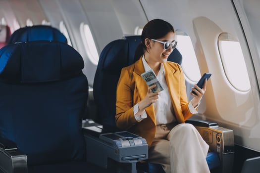 A young Asian woman, seated as an airplane passenger, contemplates dollar bills, reflecting on lucrative opportunities and aspirations towards billionaire status. photo