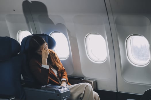 Photo of a frustrated woman sitting on an airplane with her head in her hands. Asian woman sitting in a seat in airplane