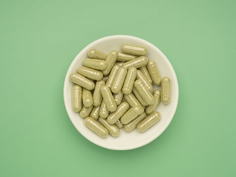 Flat lay of Andrographis capsules in a dish isolated on a green background. Space for text. Herbal, medicine, and healthcare concept photo