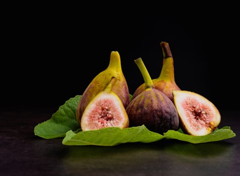 A Pile of ripe figs fruit is on green leaves on vintage with black wall background. High Vitamins fruit. Close-up photo. Healthy fruits and healthcare concept photo