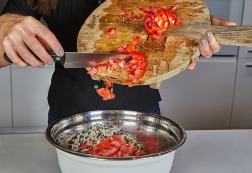 Close-up of hands throwing fresh tomatoes from a wooden cutting board into a pan with a knife in the kitchen photo