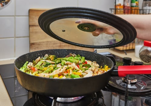 Colorful stir fry vegetables with chicken cooking in a pan on a gas stove in a home kitchen setting. photo