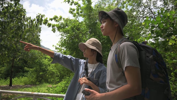 Two Asian young teen backpackers looking for directions while hiking in tropical forest park in summer holiday. Outdoor pursuits. Teenager hobbies and leisure activities. photo