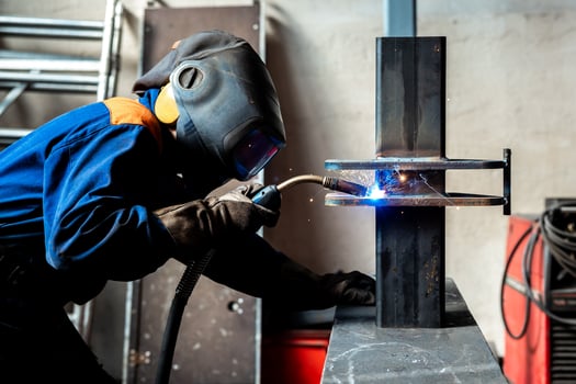 Welding work at a metalworking plant A helmeted welder welds a metal part on a welding table photo