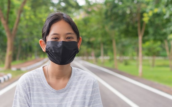 Portrait cheerful adorable Thai teen girl wears black face mask standing on the footpath in public park during COVID-19 epidemic. Healthy lifestyle. Pollution free environment. photo