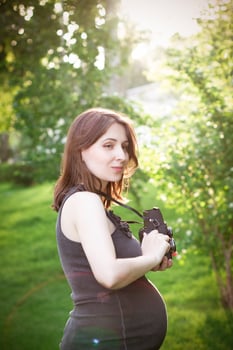 Pregnant woman with photo camera standing in park