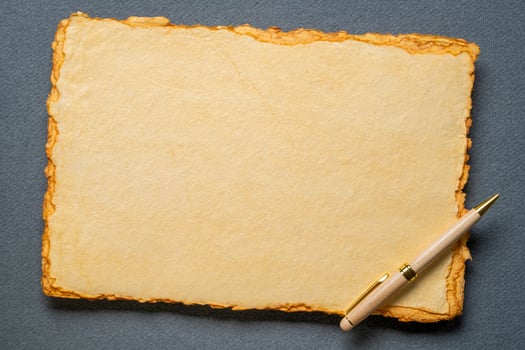 stack of tan toned heavyweight deckle edge paper sheets with a stylish pen photo