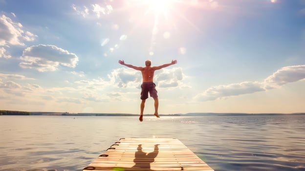 Man jumping off a wooden pier into a serene lake under a bright summer sun with a clear blue sky and fluffy white clouds photo