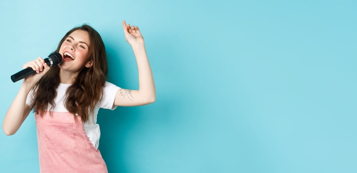 Happy young woman perform song, singer holding microphone, dancing and singing at karaoke, standing over blue background photo