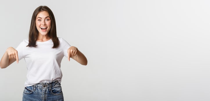 Satisfied smiling brunette girl pointing fingers down, recommend product photo