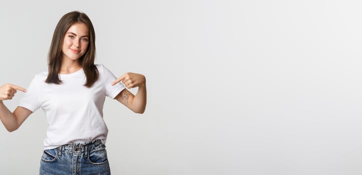 Beautiful smiling brunette girl pointing fingers at your logo, showing something on center photo