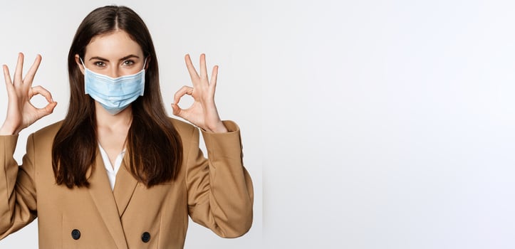 Workaplce and pandemic concept. Close up portrait of business woman showing okay signs, wearing medical mask, recommend, praise something, standing over white background photo