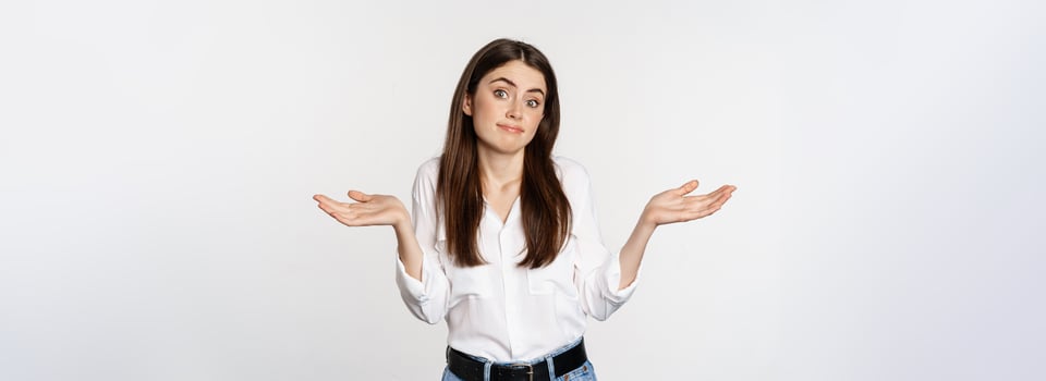 I dont know. Clueless young woman shrugging shoulders and looking unaware, standing over white background photo