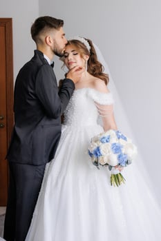 A bride and groom are kissing each other's necks. The bride is wearing a white dress and the groom is wearing a suit photo
