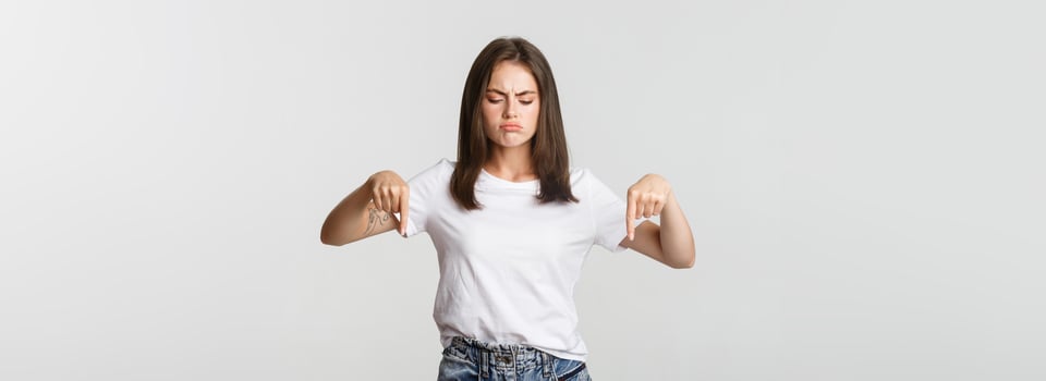 Skeptical or disappointed brunette girl complaining, pointing fingers down photo