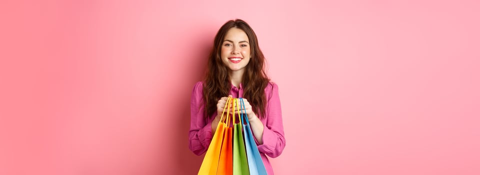 Cheerful lady standing with shopping bags, smiling and looking happy, pink background photo