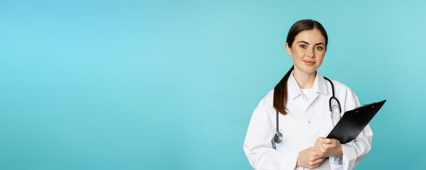 Image of professional woman doctor, physician with clipboard writing, listening patient at hospital clinic appointment, standing over torquoise background photo