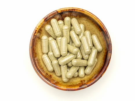 Flat lay of Andrographis capsules in a dish isolated on a white background. Space for text. Herbal, medicine, and healthcare concept photo