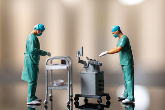 Miniature figures of healthcare professionals dressed in green surgical scrubs and masks, standing on a reflective surface. photo