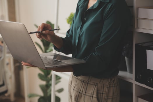 Female Manager Using Laptop Computer To Check Inventory. In the Background Warehouse Retail Center with Cardboard boxes, e-Commerce Online Orders, Food, Medicine, Products Supply. Over the Shoulder photo