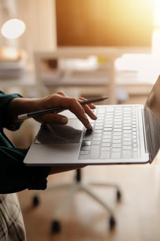 Female Manager Using Laptop Computer To Check Inventory. In the Background Warehouse Retail Center with Cardboard boxes, e-Commerce Online Orders, Food, Medicine, Products Supply. Over the Shoulder photo