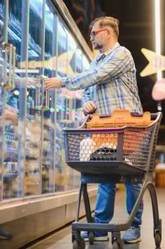 Positive adult man choosing still water in plastic bottle while shopping in supermarket photo