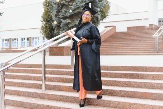 pretty african college student in graduation cap and gown in front of school building photo