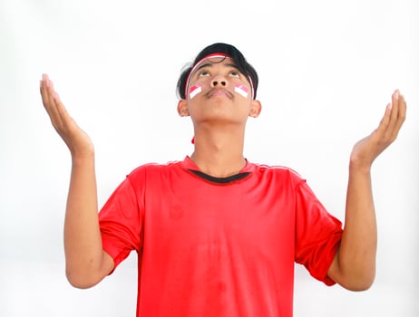 Asian Muslim man wearing independence shirt is praying and raising his head isolated on white background. Indonesian Independence day photo