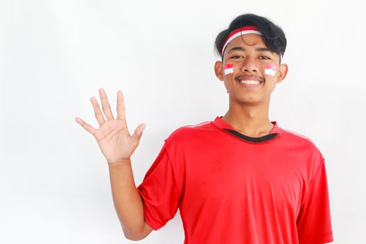 A confident young Asian man makes a number sign on an isolated white background. wearing a red shirt. Indonesian Independence day photo