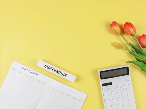 flat layout of Habit tracker book, white calculator, wooden calendar September and tulips on yellow background. photo