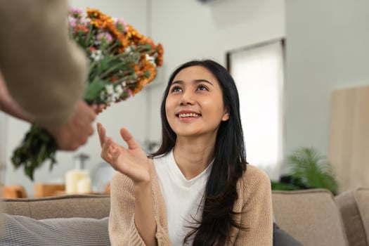 Romantic Couple at Home with Flowers, Woman Smiling and Reaching Out, Cozy Indoor Setting, Love and Happiness photo