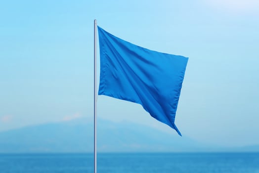 Blue flag with the sea in the background. Beaches meeting high standards are marked with a blue flag, symbolizing quality and safety. Ideal for travel and tourism photo