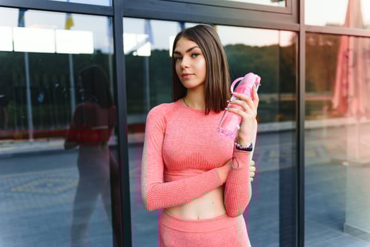 Beautiful young sporty woman drinking water after running. Fit jogger girl taking a break after sport. Lifestyle, people, sport and leisure concept. photo