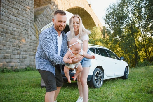 Young family three people in white clothes have picnic. Beautiful parents and daughter travel by car during summer vacation. Scene in park photo