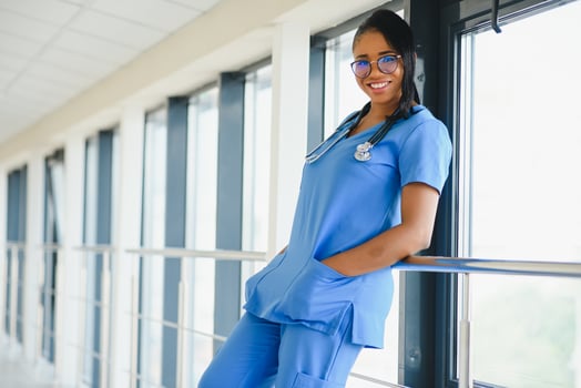 Portrait confident African American female doctor medical professional writing patient notes isolated on hospital clinic hallway windows background. Positive face expression photo