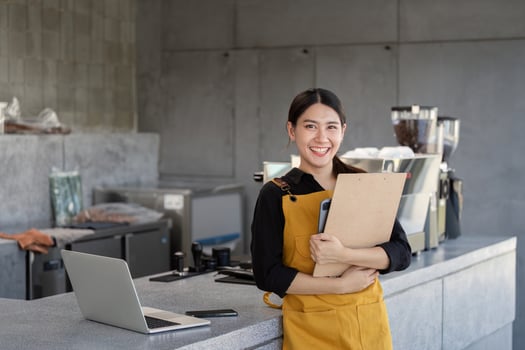 Smiling Barista Holding Clipboard in Modern Coffee Shop with Laptop on Counter photo