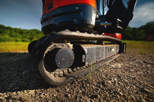 Close-up of rubber tracks of a small excavator outdoors surrounded by grass and greenery on a sunny day photo