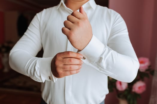 A man in a white shirt is getting dressed and adjusting his cuff. Concept of formality and attention to detail, as the man carefully straightens his shirt and cuff photo
