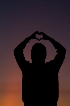 A silhouette of a young woman raising her hands above her head to represent a heart symbol signifying friendship, love and kindness. Heart symbol concept with the meaning of love and friendship. photo