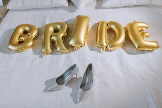 A bed with a gold lettering that says bride. There are two silver high heels on the bed photo