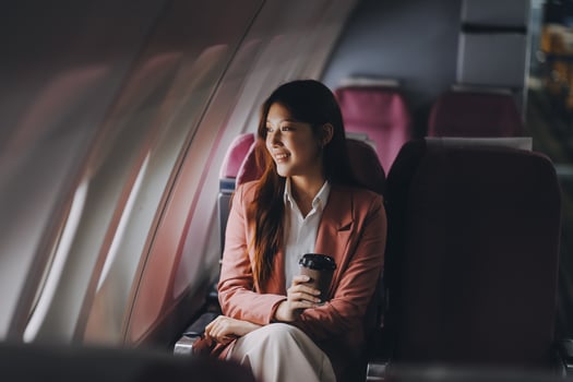Portrait of a successful Asian businesswoman or entrepreneur in a formal suit on an airplane sitting in business class using a phone, computer laptop. Travel in style, work with grace. photo