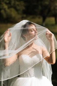 A woman wearing a white wedding dress is standing in front of a veil. She is looking at the camera with a smile on her face photo