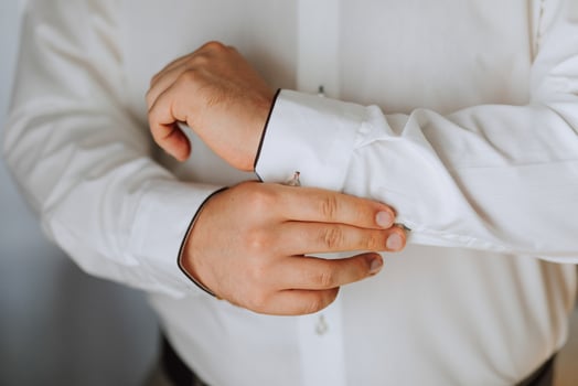 A man is getting dressed in a white shirt and black pants. He is adjusting the collar of his shirt photo